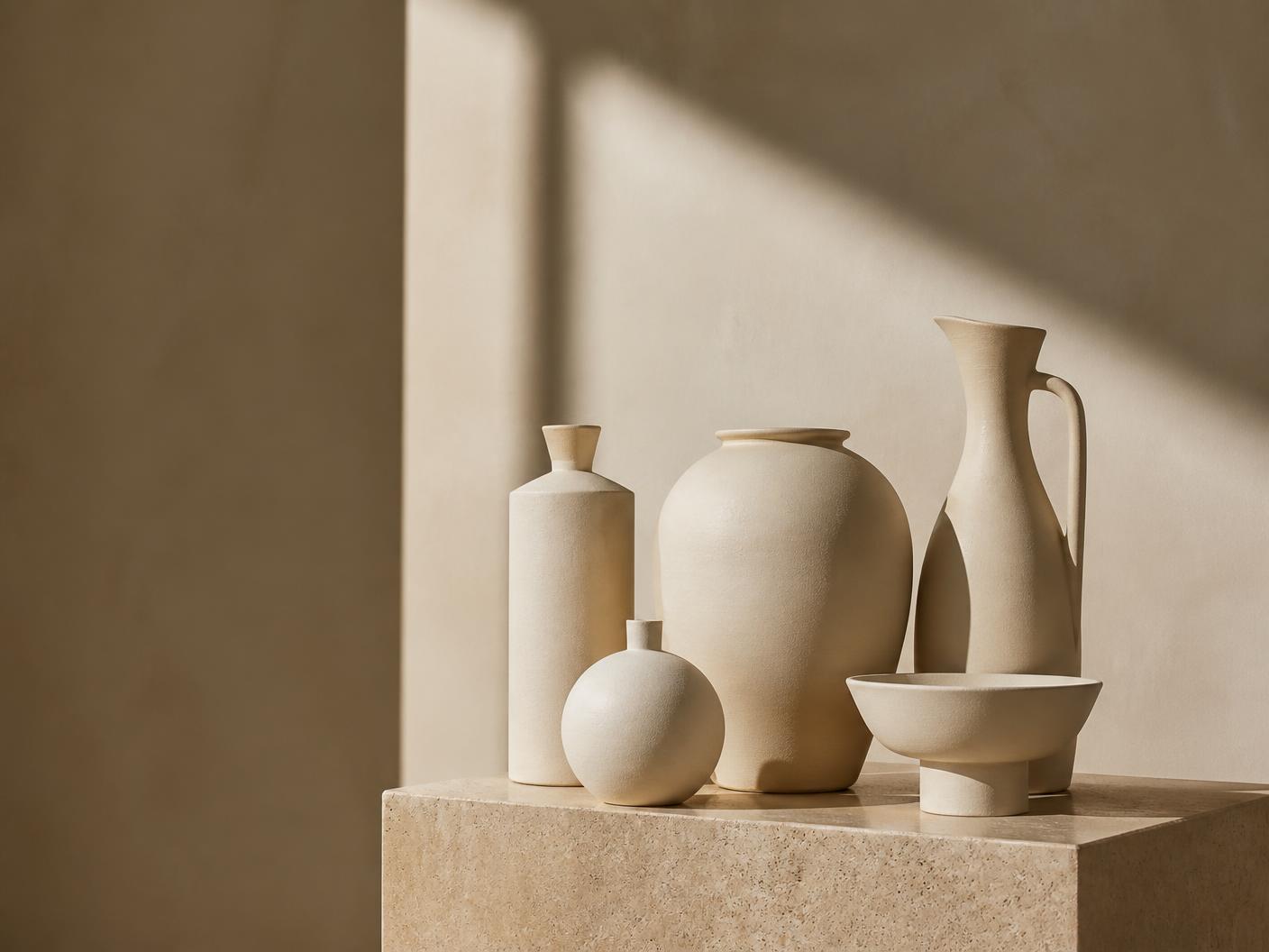 Minimal ceramic vessels in warm ivory tones on a stone plinth